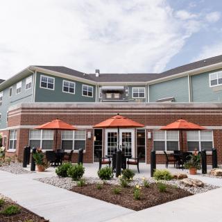 A modern residential apartment complex with outdoor seating and landscaped surroundings.