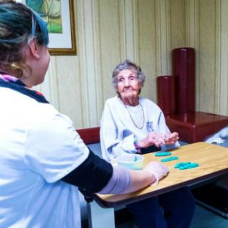 An elderly woman engages in a card game with her caregiver in a cozy indoor setting.
