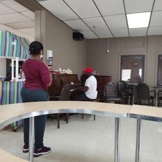 A person stands and watches as another plays the piano in a community center setting.