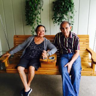 A couple sitting on a porch swing surrounded by plants.