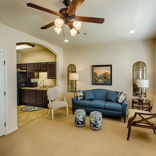 A cozy living room with a blue sofa and kitchen view, accentuated by elegant decor and a ceiling fan.