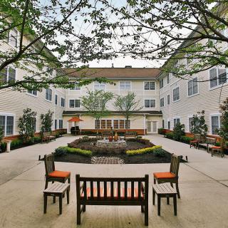 A peaceful courtyard with benches and greenery surrounded by a building.