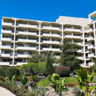 A residential apartment building with multiple balconies, surrounded by a landscaped garden and lush greenery.