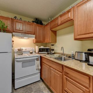 A compact kitchen with wood cabinets, appliances including a refrigerator, stove, microwave, and small countertop appliances.
