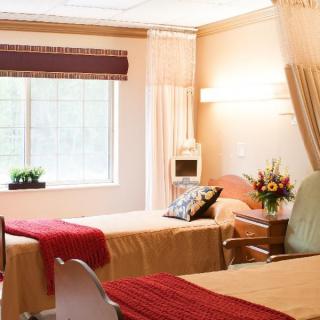 A well-lit hospital room with two patient beds adorned with red blankets, flowers, and a window view.