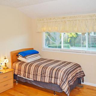 A cozy bedroom with a single bed, striped bedding, and a large window providing natural light.