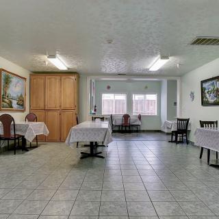 A spacious dining room with multiple tables and chairs, featuring tile flooring and paintings on the walls.