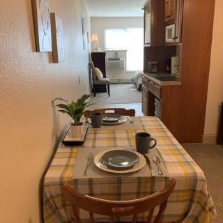 A cozy dining area with a table set for two, extending into a kitchen and living space.