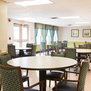A spacious and well-lit dining area featuring round tables and comfortable chairs, perfect for social gatherings.