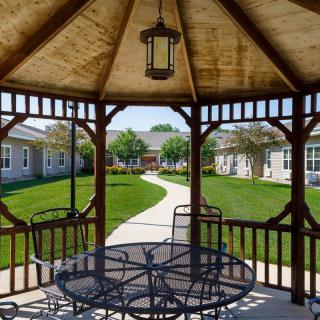 A cozy gazebo with outdoor seating overlooks a well-maintained garden and pathway.