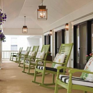 A cozy porch with green rocking chairs lined up by lanterns.