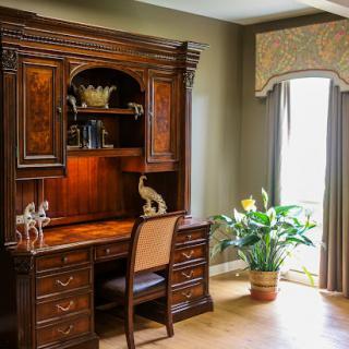 A beautifully designed home office featuring a wooden desk with an ornate shelving unit and lush indoor plants.