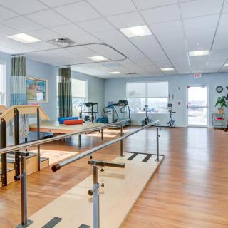 A spacious physical therapy room equipped with various exercise machines and parallel bars for rehabilitation exercises.
