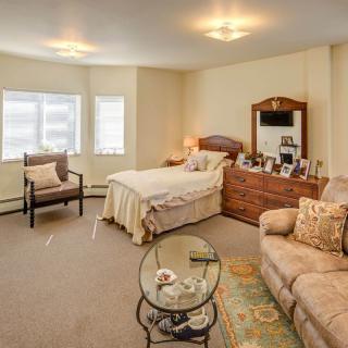 A cozy bedroom with a bed, sofa, dresser with mirror, and a small glass table.