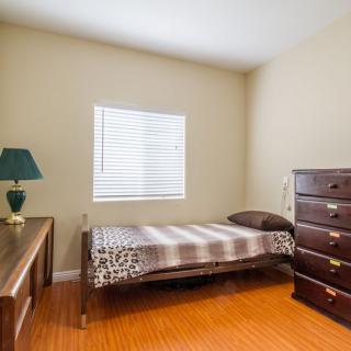 A cozy bedroom with a single bed, dresser, and desk, featuring a window with blinds.