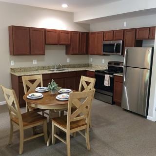 A modern kitchen and dining area featuring wooden cabinets, stainless steel appliances, and a small round dining table set with four chairs.