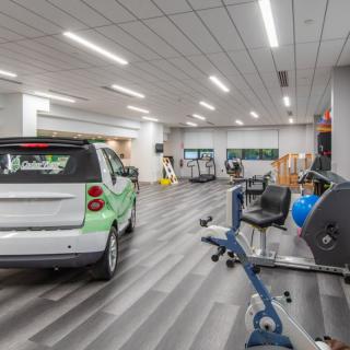 An indoor gym space featuring fitness equipment alongside a small car.