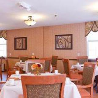 A cozy dining room with neatly arranged tables and chairs, adorned with artwork and warm lighting.