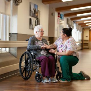 A healthcare worker assists an elderly woman in a wheelchair, showcasing compassionate care in a hospital setting.