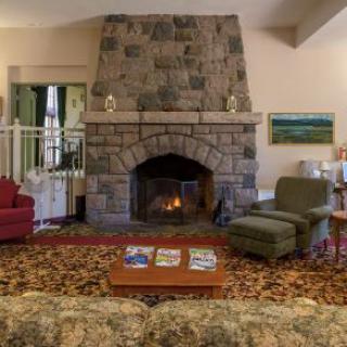 A cozy living room with a large stone fireplace, comfortable seating, and a patterned rug.