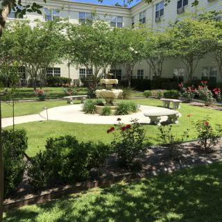 A serene courtyard garden with a central fountain, surrounded by lush greenery and benches.