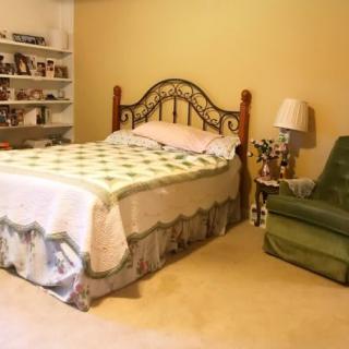 A cozy bedroom with a decorative bed, armchair, and shelves filled with items.