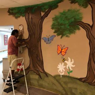 An artist adds finishing touches to a vibrant mural featuring trees, butterflies, and flowers.