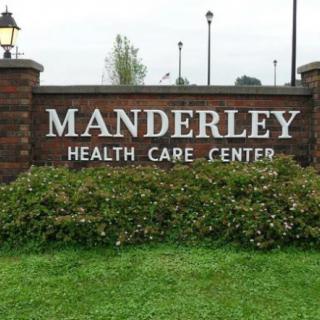 Sign for Manderley Health Care Center displayed on a brick wall with greenery.