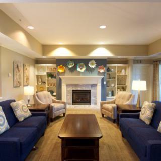 A cozy living room with a fireplace, flanked by blue sofas and armchairs, and highlighted with decorative plates on shelves.