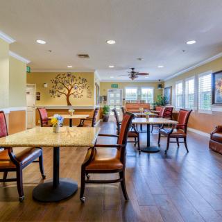 A well-lit dining room with neatly arranged tables and chairs, featuring warm decor and hardwood flooring.