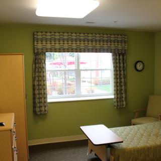 A well-lit room featuring green walls, a window with patterned curtains, and basic furniture.