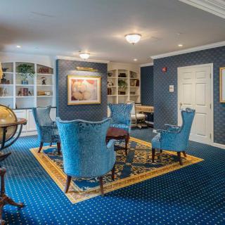 A cozy living room with elegant blue chairs and a carpeted floor, featuring bookshelves and wall art.