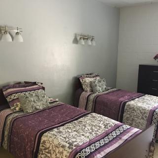 A bedroom featuring two twin beds with patterned bedding, wall-mounted lamps, and a dark dresser.
