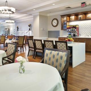 A modern dining area with elegantly set tables and chairs adjacent to a small kitchen space.