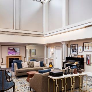 A spacious and elegant living room with modern furniture, featuring a piano and guitars, complemented by artworks on the walls.