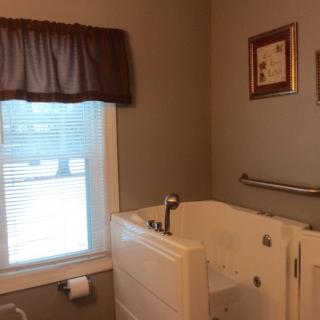 A bathroom featuring a walk-in tub with a window, curtain, and framed art on the wall.