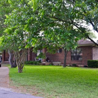 A suburban brick house with a lush green lawn and driveway.