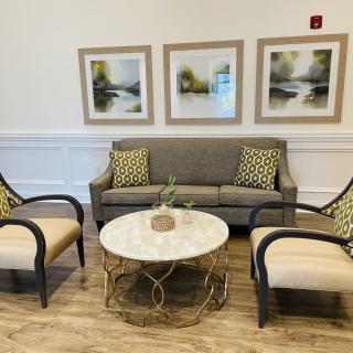 A cozy seating area with a gray sofa, two armchairs, and a round coffee table, adorned with nature-themed artwork on the wall.