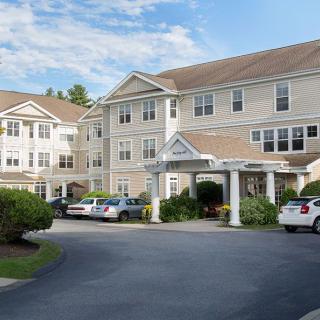 A view of a multi-story residential building with cars parked in the driveway.