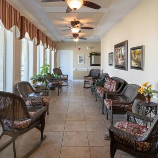A well-lit waiting room featuring comfortable seating, ceiling fans, potted plants, and decorative artwork along the walls.