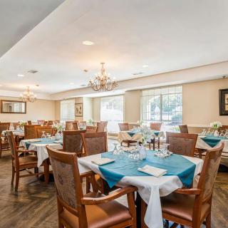A well-decorated dining room with neatly arranged tables, each adorned with teal tablecloths and elegant place settings, under a large chandelier.