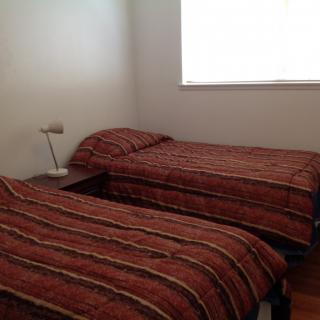 A simple bedroom with twin beds and a lamp by the window.