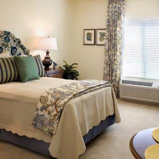 A cozy and well-decorated bedroom featuring a bed with patterned pillows, a lamp on the bedside table, and a window with curtains allowing natural light to brighten the space.