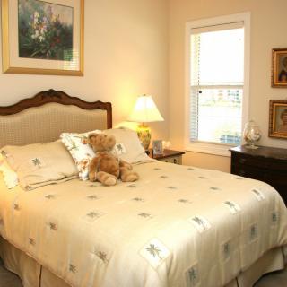 Cozy bedroom with a neatly made bed adorned with a teddy bear, warm lighting, and classic decor.