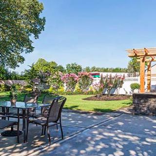 A beautiful outdoor patio area featuring garden furniture, lush greenery, and a wooden pergola.
