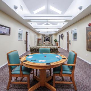 A central poker table with chairs in a brightly lit hallway setting.