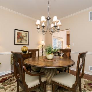 A cozy dining room featuring a round wooden table with chairs, illuminated by an elegant chandelier.