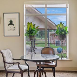 A cozy interior scene featuring a round table, stylish chairs, and vibrant plants by a large window.