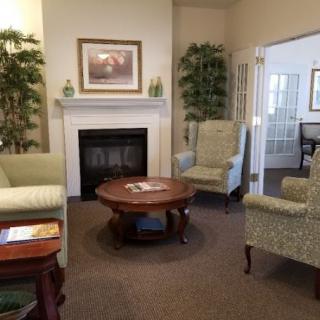 A cozy living room with a fireplace, armchairs, and a coffee table surrounded by decorative plants.