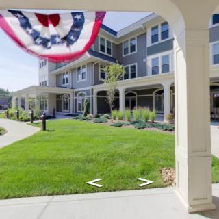 An exterior view of a modern apartment building with a well-maintained lawn and a patriotic banner hanging from the porch.